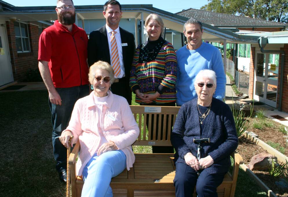 In memory: HDRC Services dementia respite care clients, Merlene Wright (left, seated) and Joyce Barry, both of Port Macquarie, on the garden bench seat carrying the plaque in memory of the late John Jordan. At rear (from left) are Bunnings’ store manager, Brett Owen, and Laing+ Simmons’ Andrew Meldrum with HDRC Board member Pat Thoeret and CEO, Raymond Gouck.