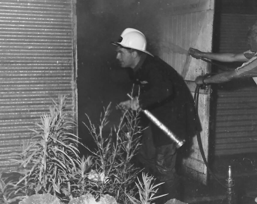 On the job: A visiting fireman on holidays uses a garden hose to douse the Co-op fire whilst local fireman Ian Anderson waits for water.