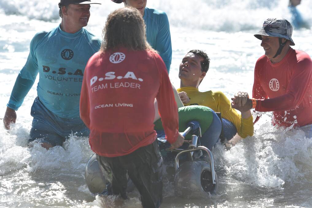 Sense of safisfaction: Volunteers help a disabled surfer in the waves at Flynns Beach.