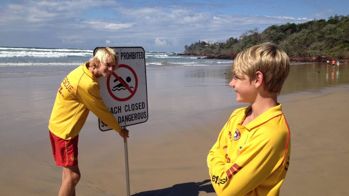 Paul Jamieson placing beach closed sign at Rainbow Beach as Brady Hoole keeps check of the surf on Saturday.