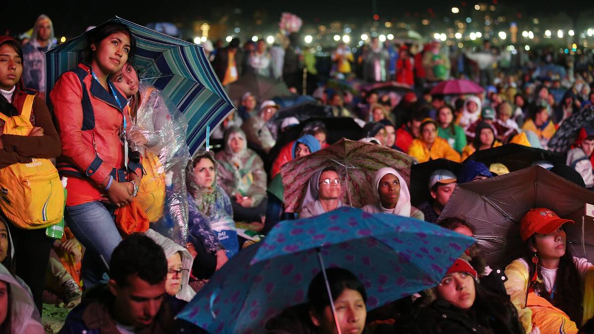 People watch a video screen in a light rain as Pope Francis celebrates Mass on Copacabana Beach on July 25. Photo: Getty Images