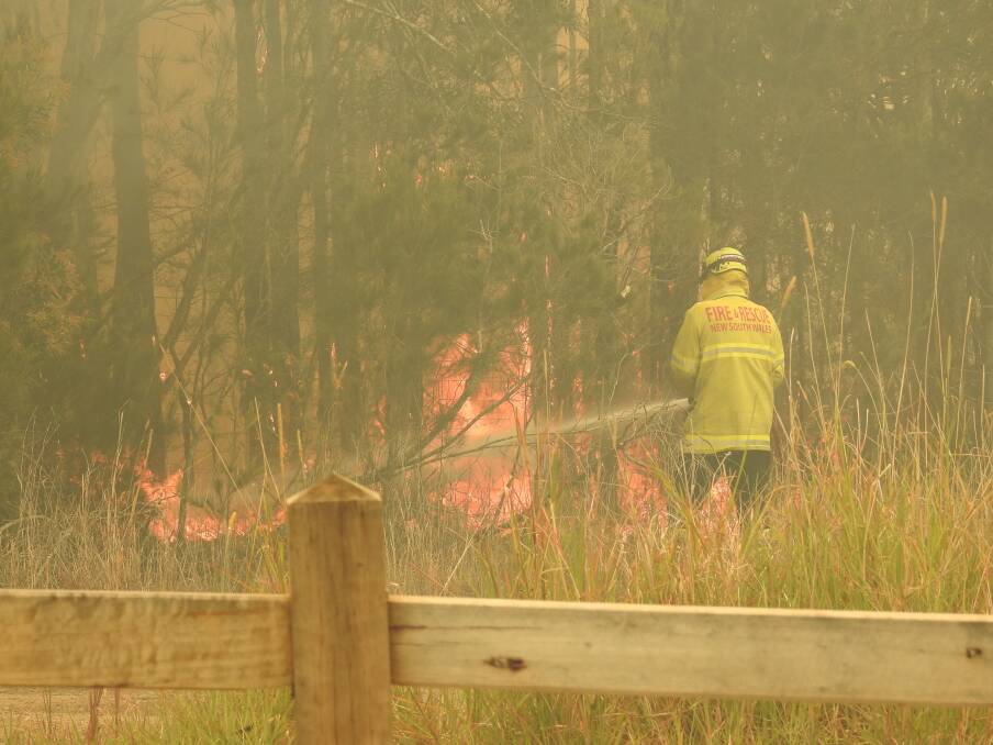 An RFS firefighter hosing flames on the edge of College Rise in Thrumster at Seminar Street. Photo: Letitia Fitzpatrick.