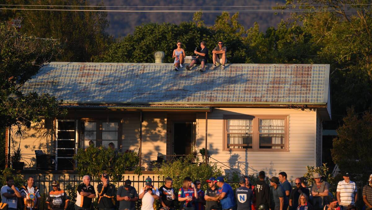 Vantage point: Spectators are seen watching on from the roof of a house during the NRL match between the Wests Tigers and the Newcastle in Tamworth. Photo: AAP/Dan Himbrechts.