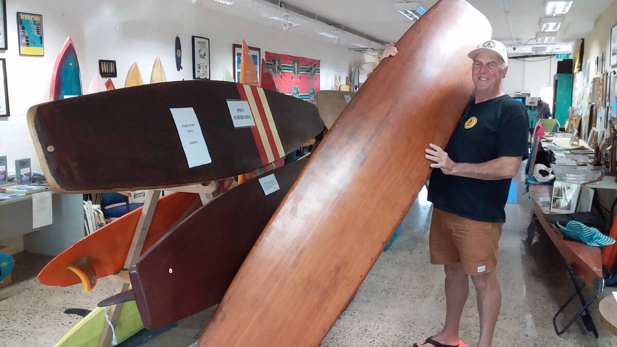 Jim Cain holding his recent purchase of a 1940s solid timber 14 foot Ockanui surfboard. This board is on display at the Museum and complements other similar old timber boards.