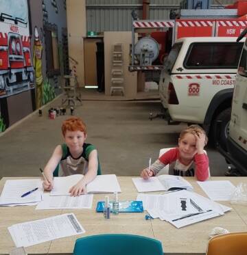 HARD AT WORK: Tyler and Riley Moroney completing school work as the mural takes shape in Wauchope.