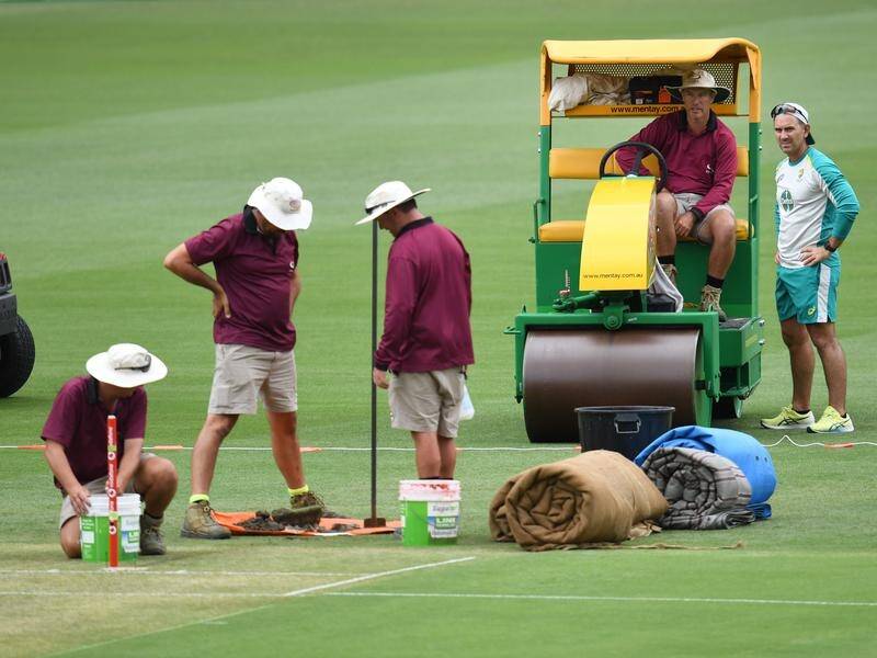 Australia coach Justin Langer (R) looks on as the Gabba ground staff Gabba prepare the wicket.